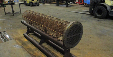 Industrial shell and tube heat exchanger component in a workshop, showing cylindrical tube bundle mounted on a metal support frame.